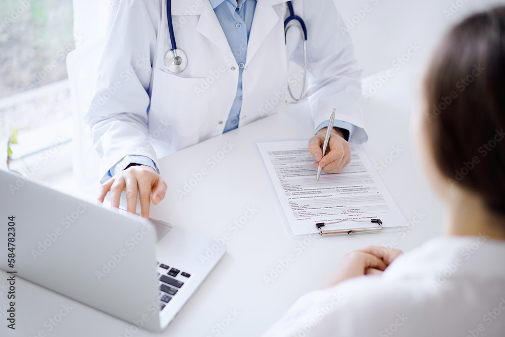 Doctor and patient discussing something and using laptop while sitting opposite each other at the desk in clinic office. Perfect medical service and medicine concept Doctor and patient discussing something and using laptop while sitting opposite each other at the desk in clinic office. Perfect medical service and medicine concept