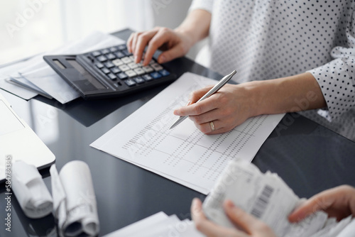 Woman accountant using a calculator and laptop computer while counting taxes for a client. Business audit and finance concepts