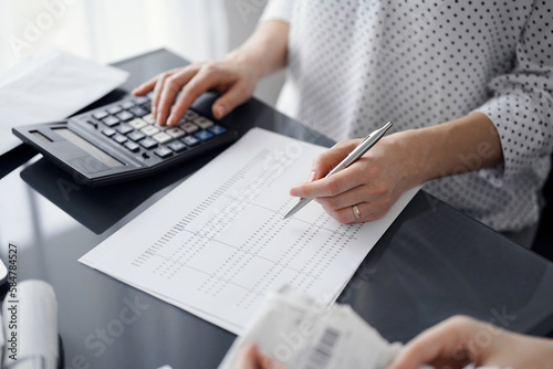 Woman accountant using a calculator and laptop computer while counting taxes for a client. Business audit and finance concepts