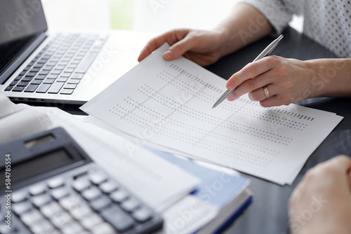 Female accountant pointing with a pen into audit paper while explaining tax counting results, close up. Business audit and finance concepts