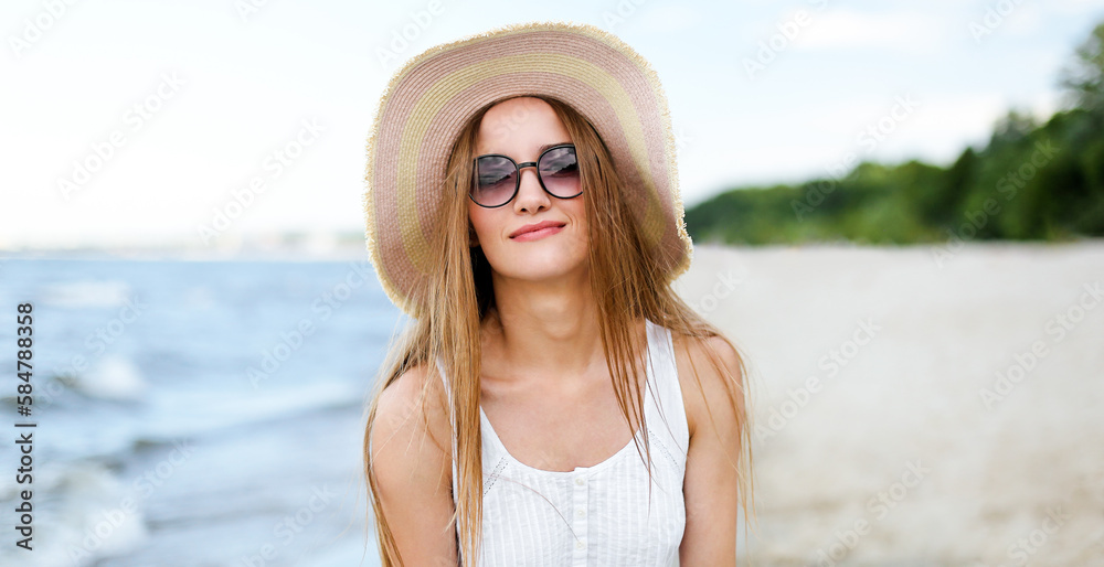 Happy smiling woman in free happiness bliss on ocean beach standing and posing with hat and sunglasses. Portrait of a female model in white summer dress enjoying nature during travel holidays vacation