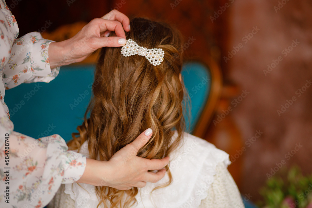 Fototapeta premium Vinnytsia, Ukraine. March 20: A mother makes her daughter's hairstyle for her long hair. White hairpin. Mother's Day