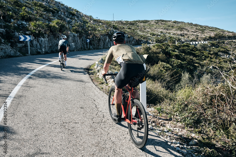 Two cyclists training on Vall d'Ebo pass.Cycling in the spanish mountains.Cyclists in helmets and cycling wear conquer Vall d'Ebo pass.Sport motivation.Cycling professional group ride.Beautiful view. Two cyclists training on Vall d'Ebo pass.Cycling in the spanish mountains.Cyclists in helmets and cycling wear conquer Vall d'Ebo pass.Sport motivation.Cycling professional group ride.Beautiful view.