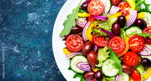 Vegan greek salad with kalamata olives, red tomato, yellow paprika, cucumber and onion, healthy mediterranean diet food, low calories eating. Blue stone background, top view. Close-up banner