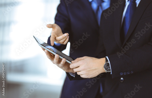Business people use a tablet computer for discussion of their new project, standing in a modern office. Unknown businessman or male entrepreneur with a colleague at workplace. Teamwork concept