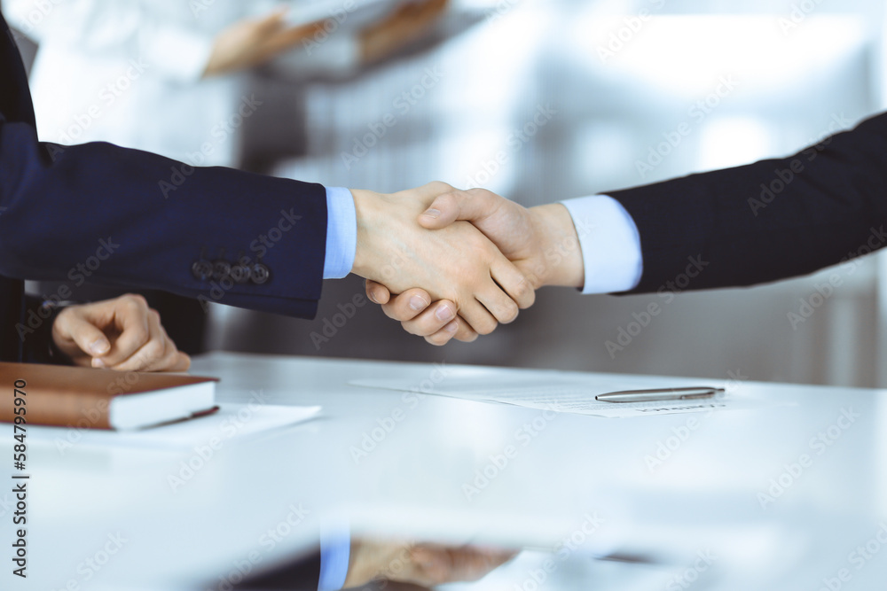 Business people shaking hands at meeting or negotiation, close-up. Group of unknown businessmen sitting at the desk in a modern office. Teamwork and partnership concept
