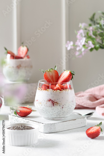 Chia pudding in a glasses with strawberries and oatmeal. White background, spring flowers.