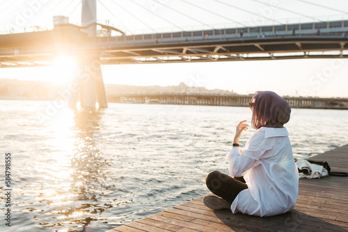 Woman fixing her scarf while sitting on shore and enjoying photo