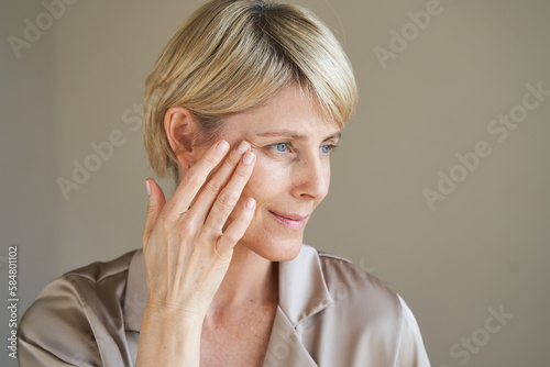 Middle aged woman applying cream on eye wrinkles photo