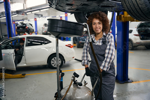 Billede på lærred Young auto repair worker with special reservoir for draining brake fluid