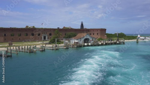 Fort Jefferson Boat Dock and house at Dry Tortugas National Park. A boat's wake, boat dock, brick fort, Garden Key Harbor Light lighthouse. Largest masonry fort in the Florida Keys was unfinished.
