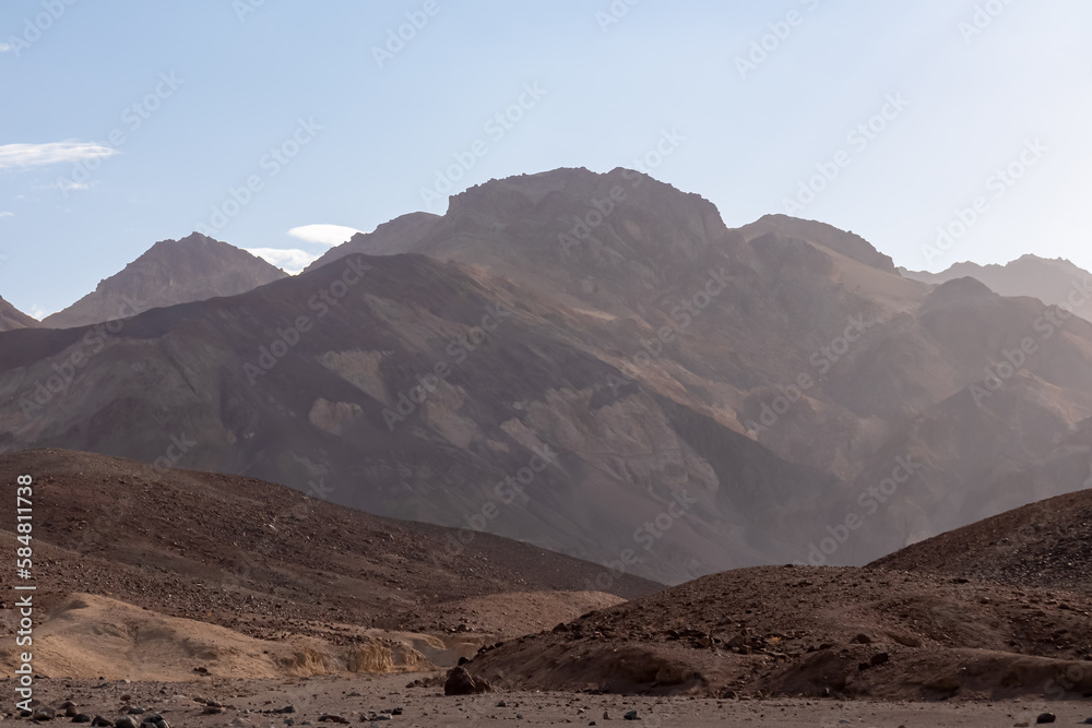 Panoramic sunrise view of the silhouette of Black, Amargosa and Panamint Mountain Range in Death Valley National Park, California, USA. Hot air and morning atmosphere in the Mojave desert. Sunbeams