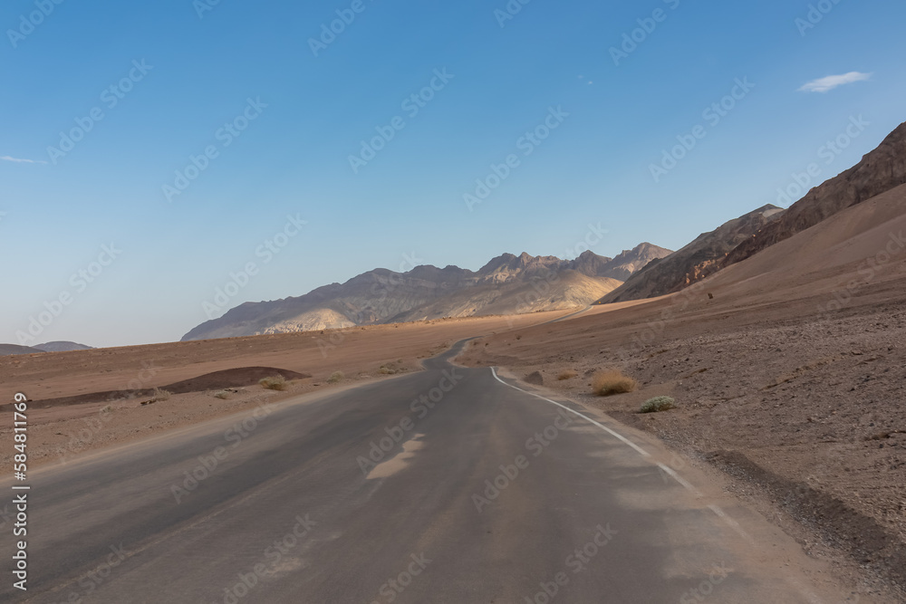 Panoramic view of endless empty road leading to colorful geology of multi hued Artist Palette rock formations in Death Valley National Park near Furnace Creek, California, USA. Black mountains