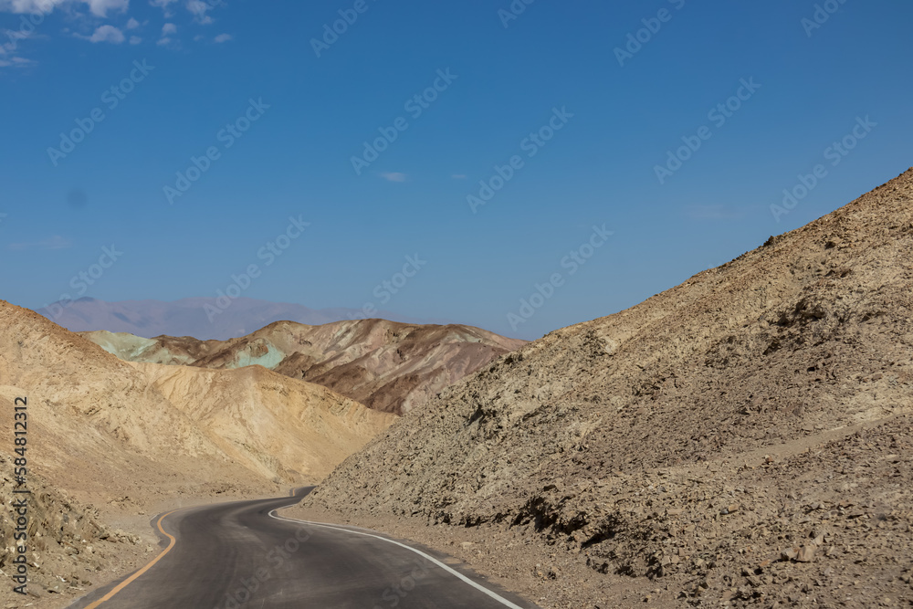 Panoramic view of endless empty road leading to colorful geology of multi hued Artist Palette rock formations in Death Valley National Park near Furnace Creek, California, USA. Black mountains