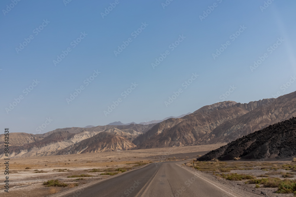 Panoramic view of endless empty road leading to colorful geology of multi hued Artist Palette rock formations in Death Valley National Park near Furnace Creek, California, USA. Black mountains