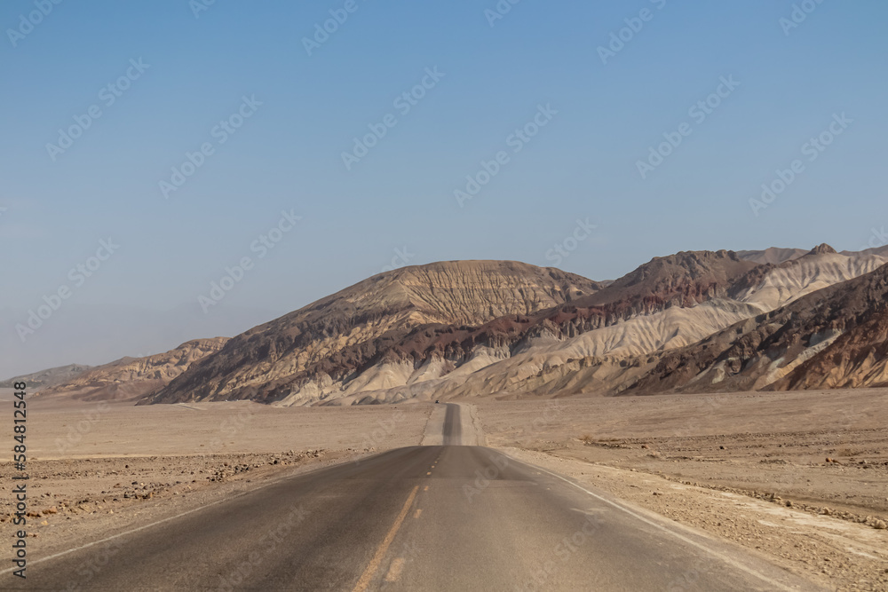 Panoramic view of endless empty road leading to colorful geology of multi hued Artist Palette rock formations in Death Valley National Park near Furnace Creek, California, USA. Black mountains