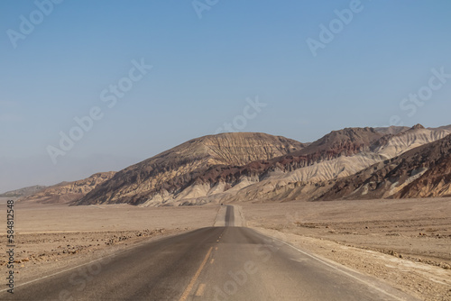 Panoramic view of endless empty road leading to colorful geology of multi hued Artist Palette rock formations in Death Valley National Park near Furnace Creek  California  USA. Black mountains