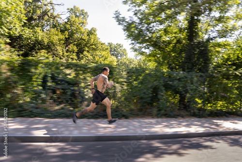 Full length of tattooed man jogging near green forest photo