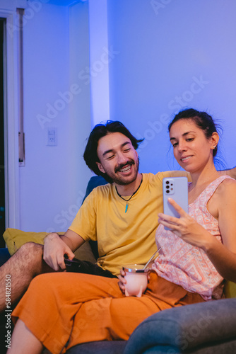 Young latin couple making a video call through their smart phone while sharing a mate. Vertical photo.