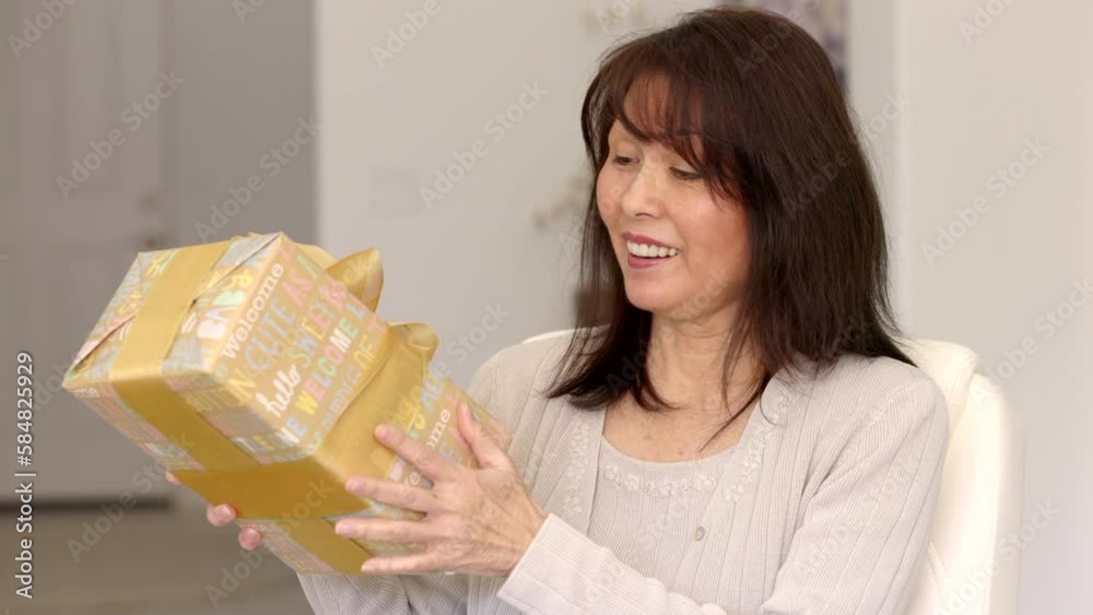 Attractive mature woman with cheerful face looking at birthday present with colorful wrapping Attractive mature woman with cheerful face looking at birthday present with colorful wrapping