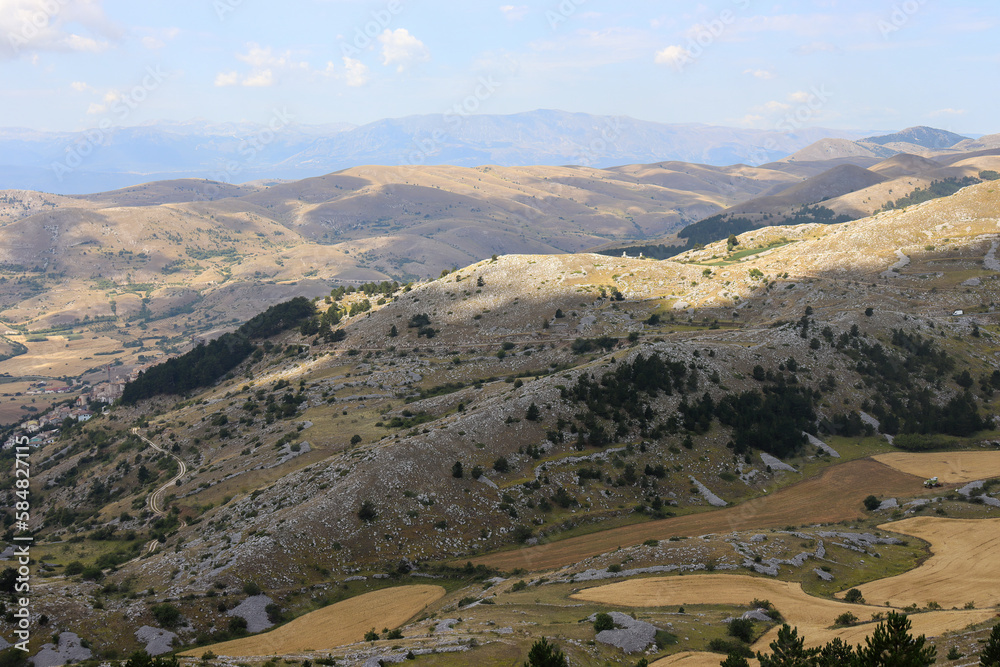 View of a mountain landscape with meadow, trees, steppe and buildings in Abruzzo in summer in Italy