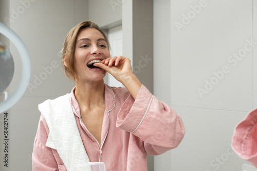 Happy woman using dental retainer in bathroom