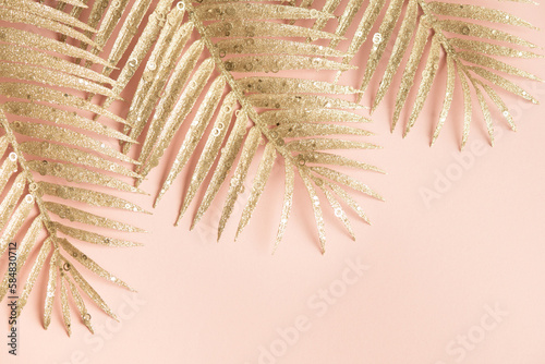 Golden palm leaves on a light pink background. Leaves with sparkles close up. Three palm branches diagonally.