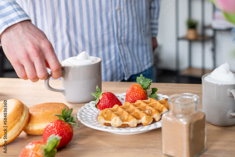 The crispy waffles, red strawberries on a beautiful white plate. Donuts, strawberries, a bowl of cinnamon, coffee with whipped cream in cups. Coffee advertising