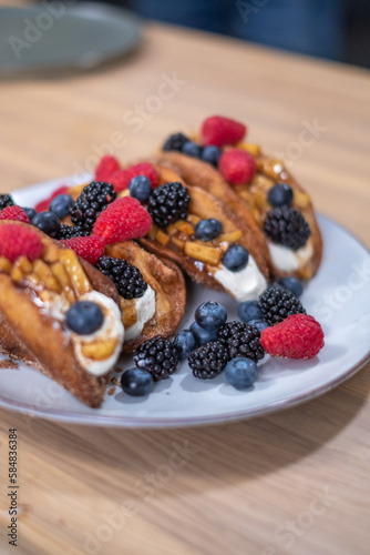 The freshly baked, large brown sweet rolls with cream cheese and fresh blueberries, strawberries, raspberries and currants on a white plate on wooden table