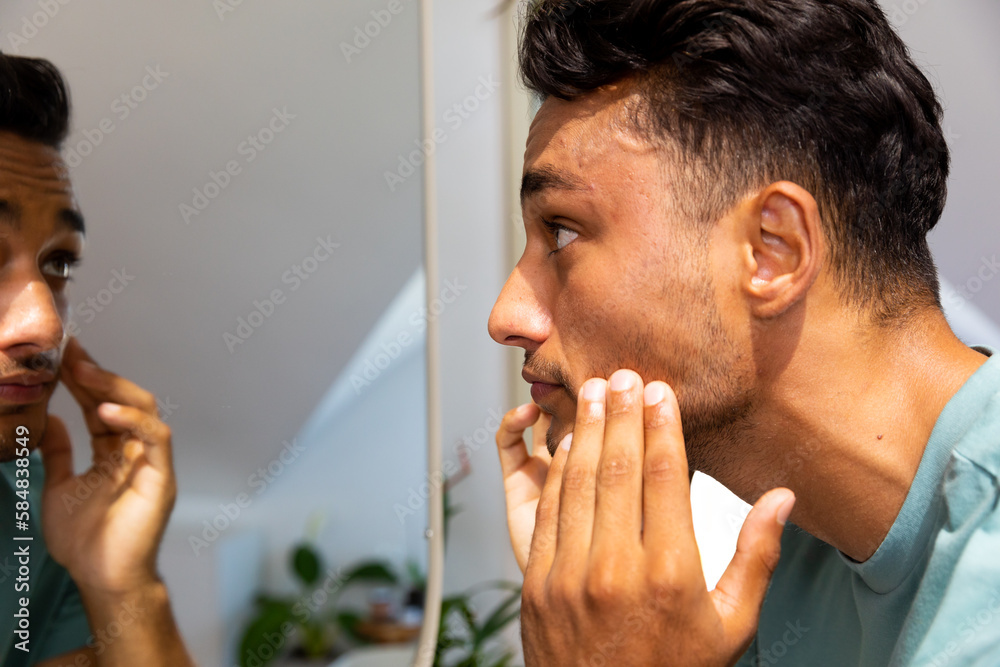Biracial man touching his face, looking at himself in bathroom mirror Biracial man touching his face, looking at himself in bathroom mirror