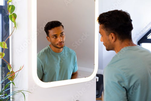 Biracial man looking at himself in bathroom mirror