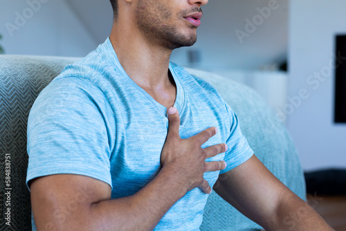 Midsection of biracial man sitting on floor in bedroom, meditating with deep beathing photo