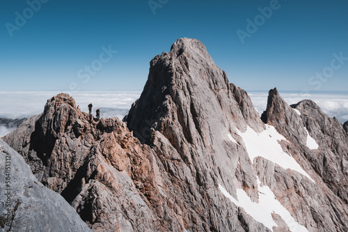 Two climbers doing the rock ridge of Cabrones-Cerredo in Picos de Europa, over a sea of clouds.