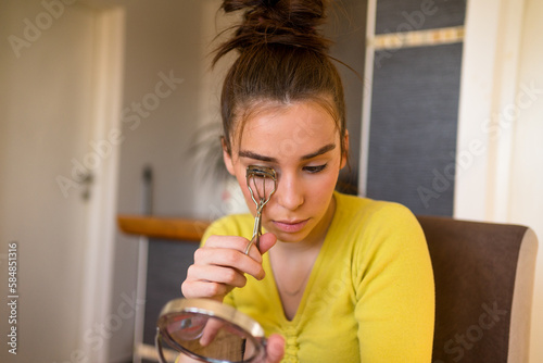 Young woman using eyelash curler at home.