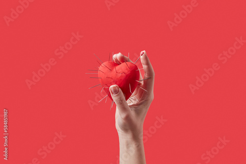 Red heart with metal spikes held by female hand. photo