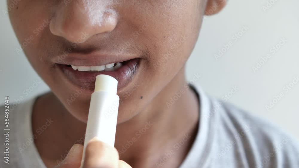 young man applying moisturising lip balm on lips young man applying moisturising lip balm on lips