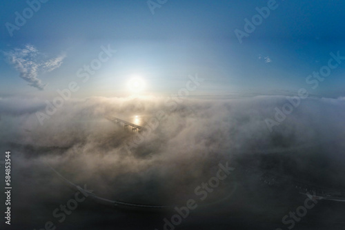 Skyview of bridge passing through clouds and a sunrise