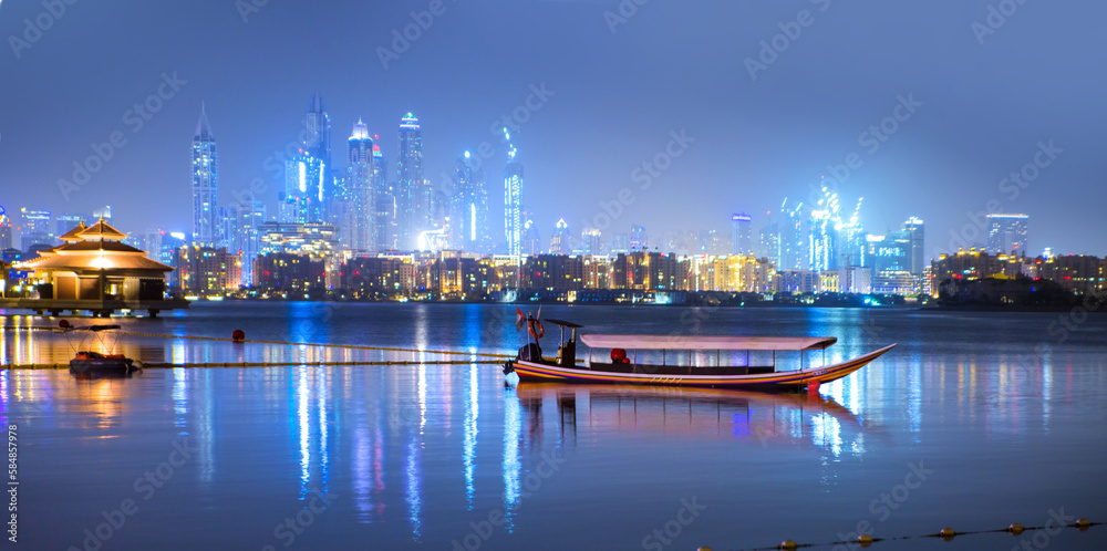Beautiful night view at Dubai Marina from the Palm Jumeirah with traditional boat at night. Dubai, UAE