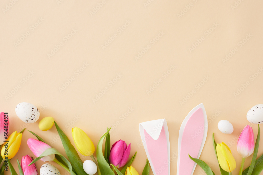 Easter concept. Flat lay composition of rabbit bunny ears pink yellow tulips flowers and colorful easter eggs on isolated beige background with copyspace