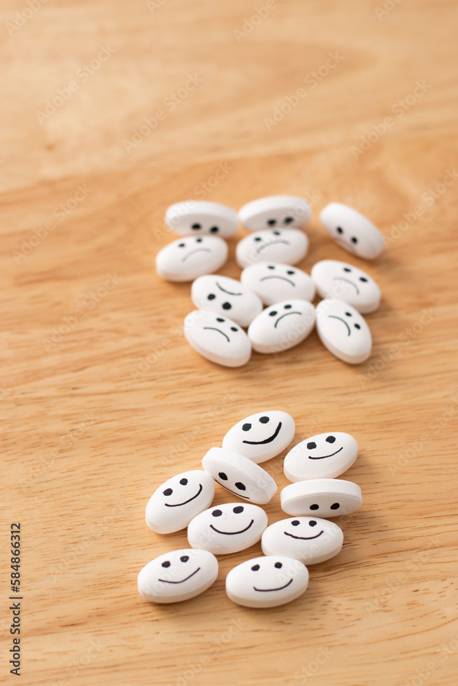 Vertical view of medicine pill with happy and sad faces over table of ...