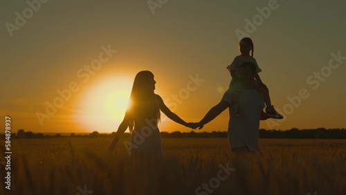 Little daughter, father mother travel, play, enjoy nature outdoors, dream, sunset. Happy family of farmers with child walks through wheat field in sun. Slow motion. Mom, dad, kid are walking together