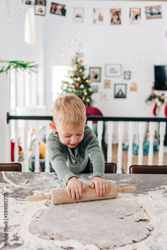 A toddler boy rolls out gingerbread dough in a cozy kitchen