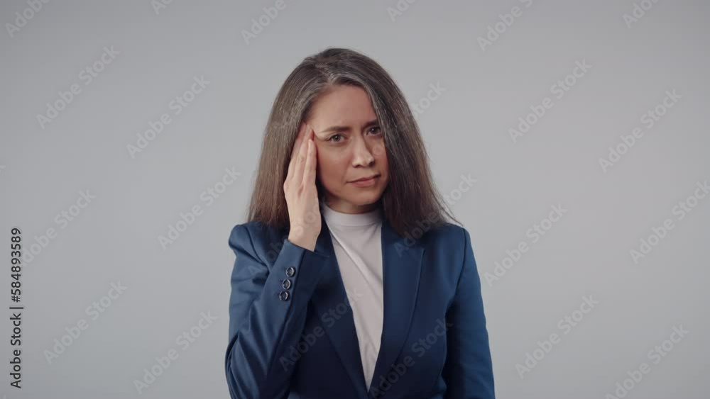 Attractive middle aged caucasian brunette business woman wearing jacket feels headache standing on grey background, tired female office manager feels migraine, studio shot Attractive middle aged caucasian brunette business woman wearing jacket feels headache standing on grey background, tired female office manager feels migraine, studio shot