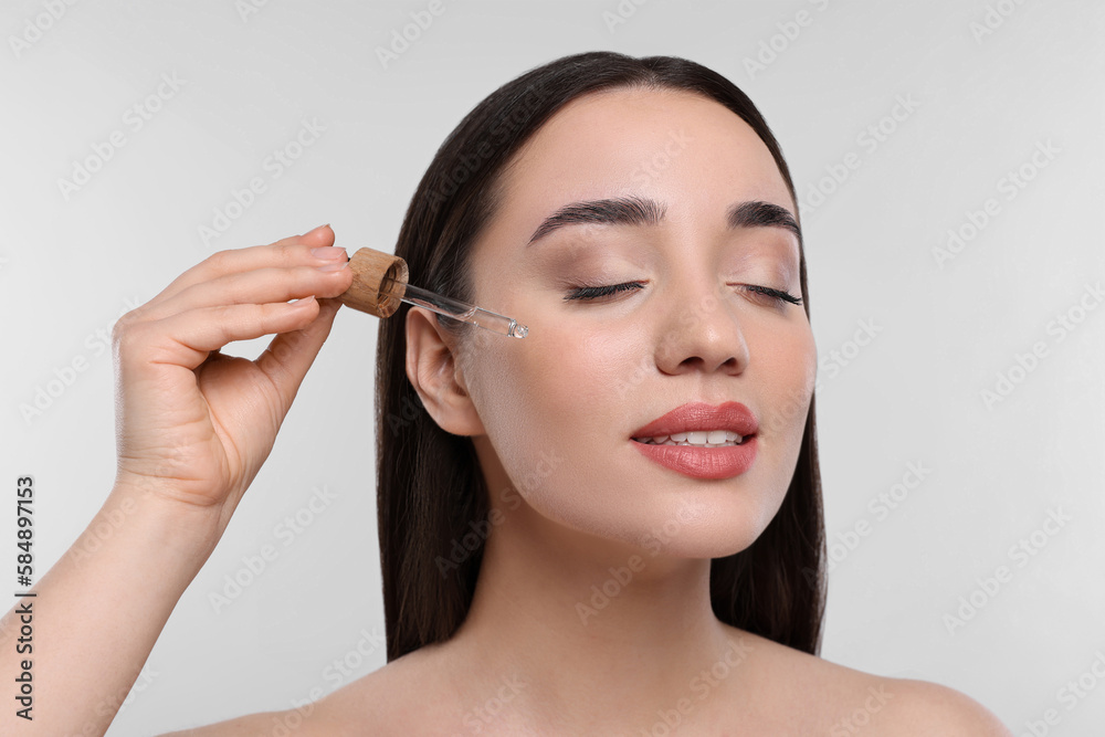 Young woman applying essential oil onto face on white background, closeup