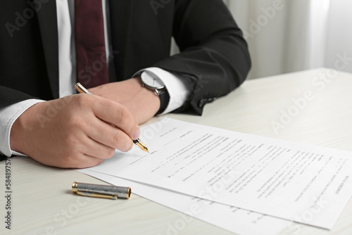 Notary signing document at wooden table, closeup