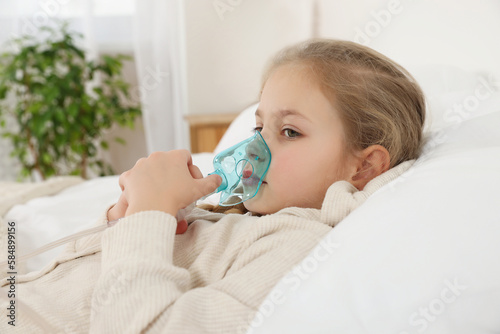 Little girl using nebulizer for inhalation in bedroom photo