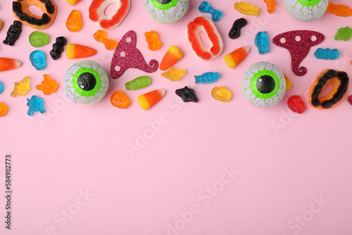 Tasty colorful jelly candies and Halloween decorations on pink background, flat lay. Space for text
