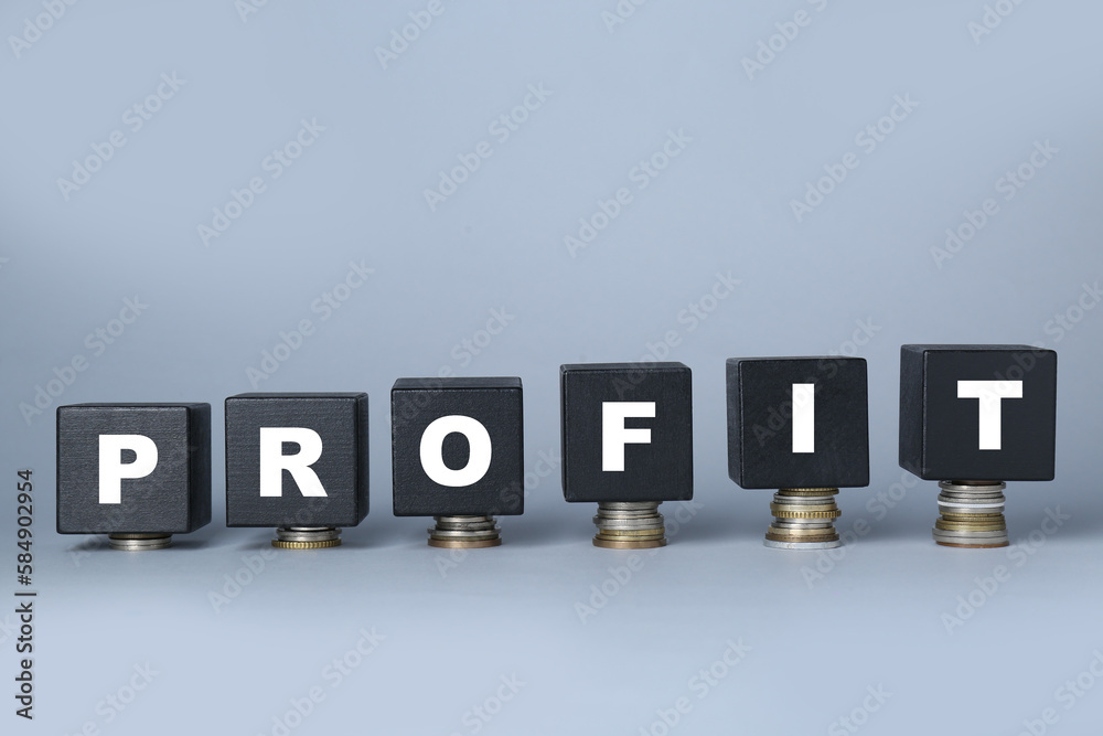 Black wooden cubes with word Profit on stacked coins against light grey background Black wooden cubes with word Profit on stacked coins against light grey background