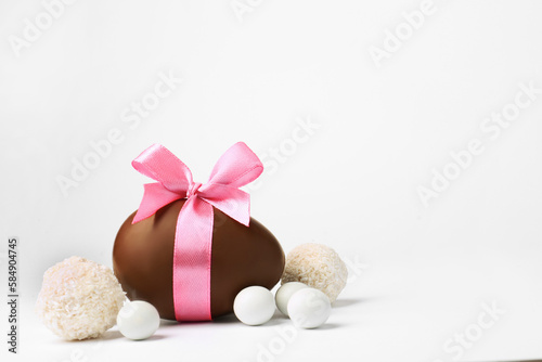 Sweet chocolate egg with pink bow and different candies on light background, space for text