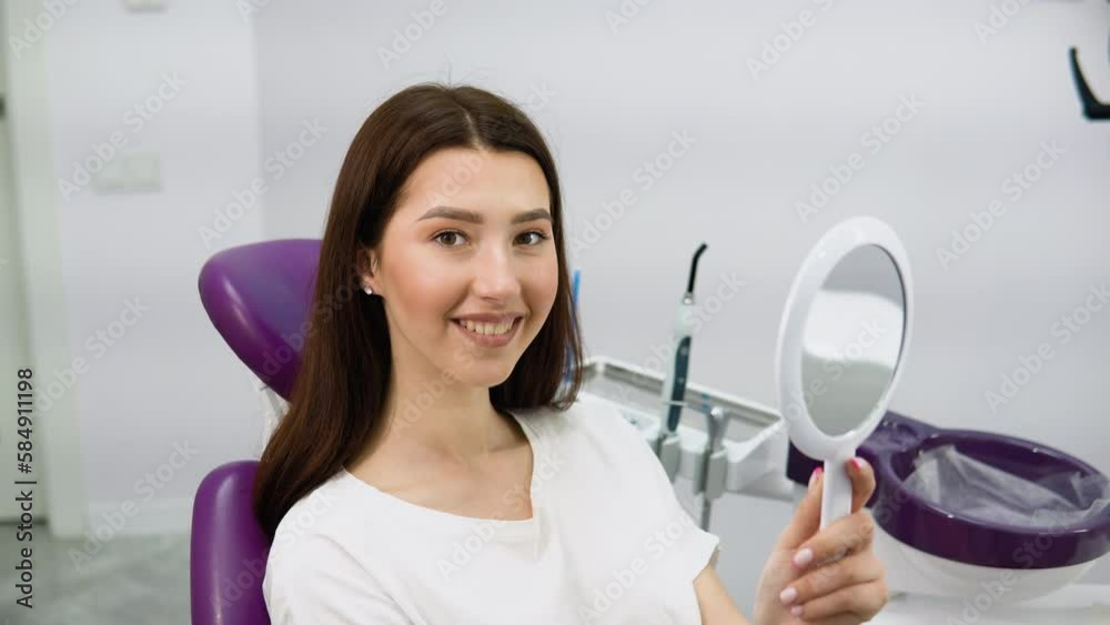 Beautiful young woman looking at mirror with smile in dentistry. Now my smile is perfect Beautiful young woman looking at mirror with smile in dentistry. Now my smile is perfect